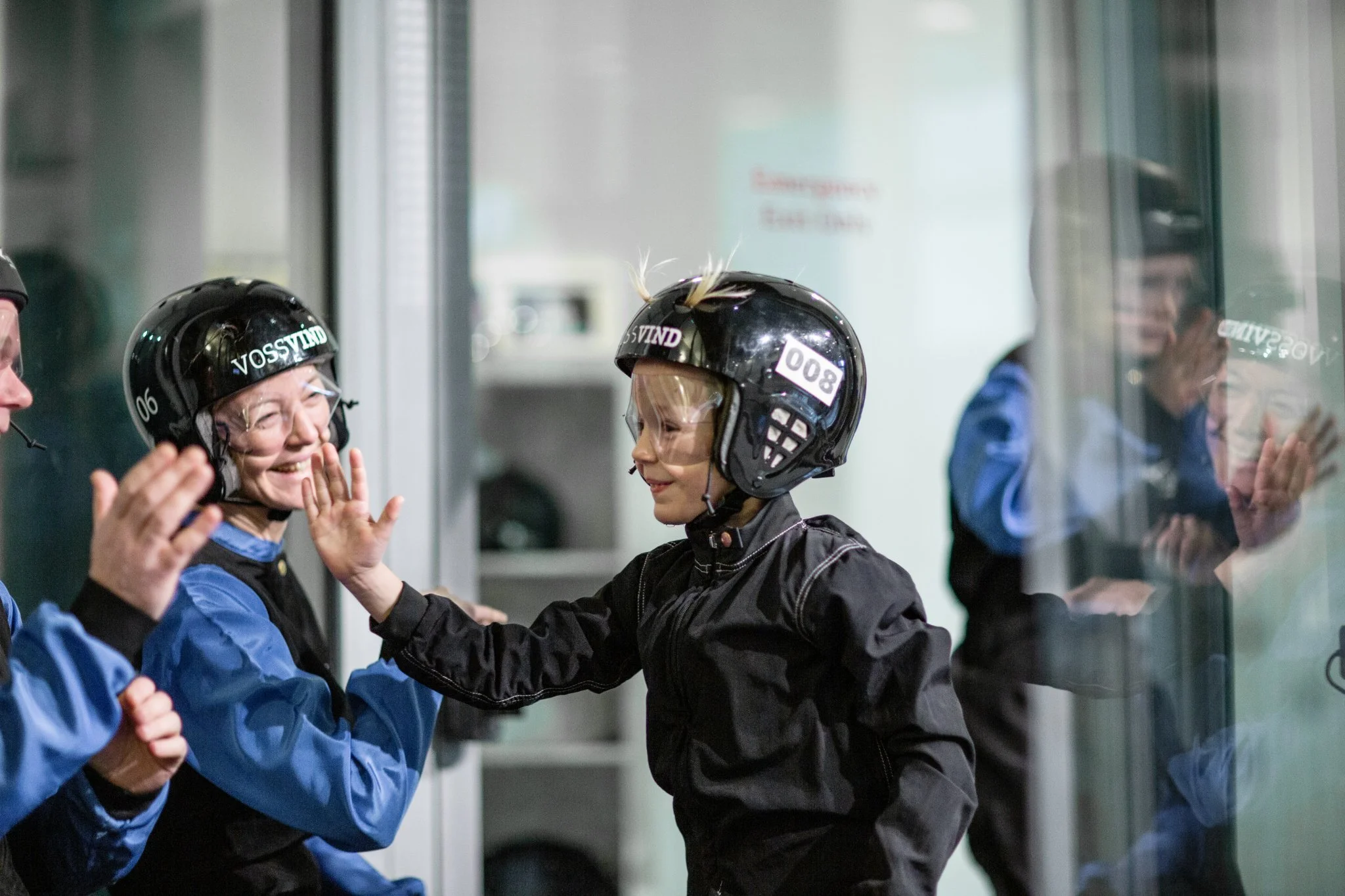 Smilende barn i hjelm gir et high five til voksen i hjelm, med refleksjoner av dem i glasset.