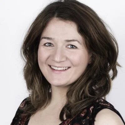 Portrett av smilende kvinne med brunt hår, mot en hvit bakgrunn.