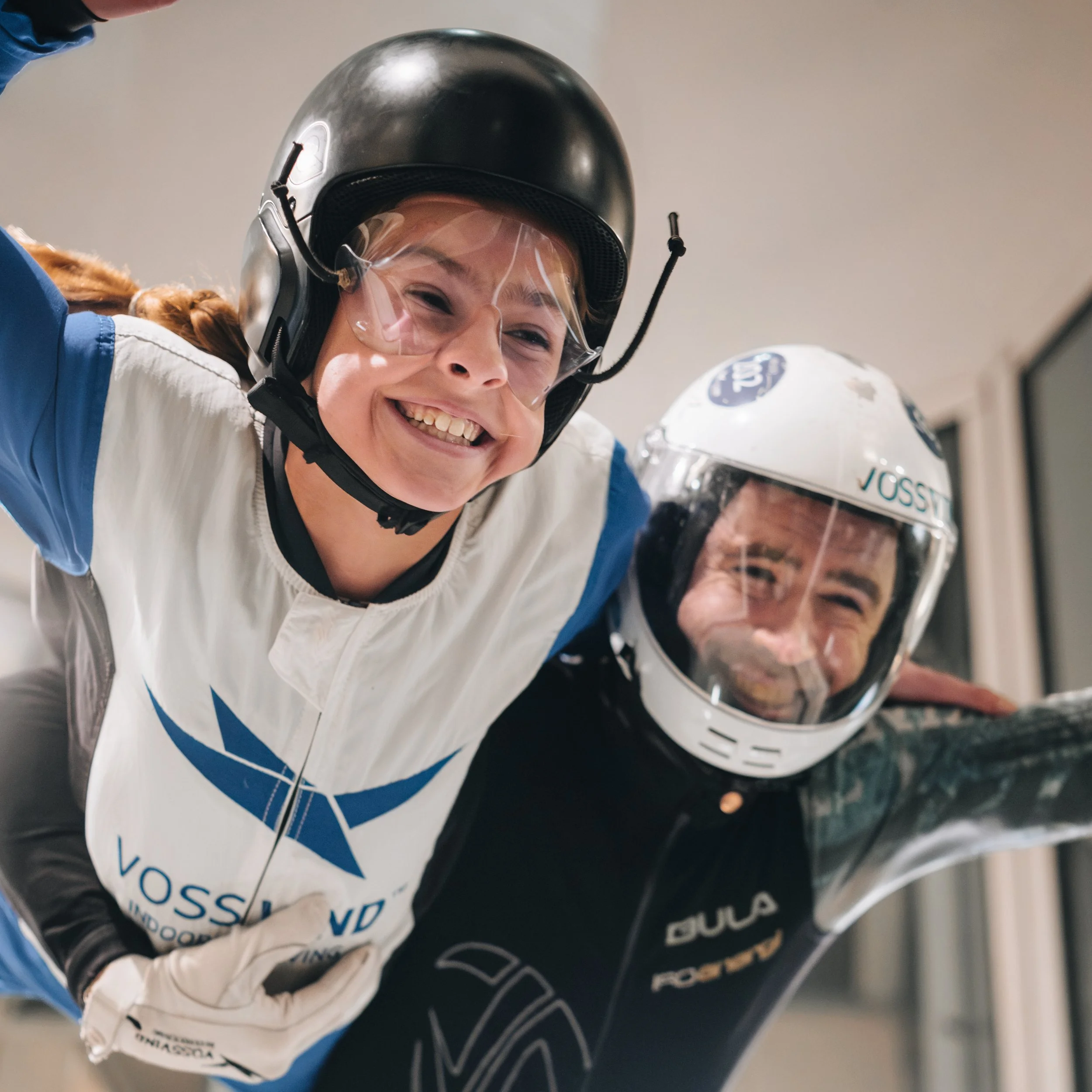 To personer flyr i vindtunell. Smiler mot kamera. Instruktør og ung jente.