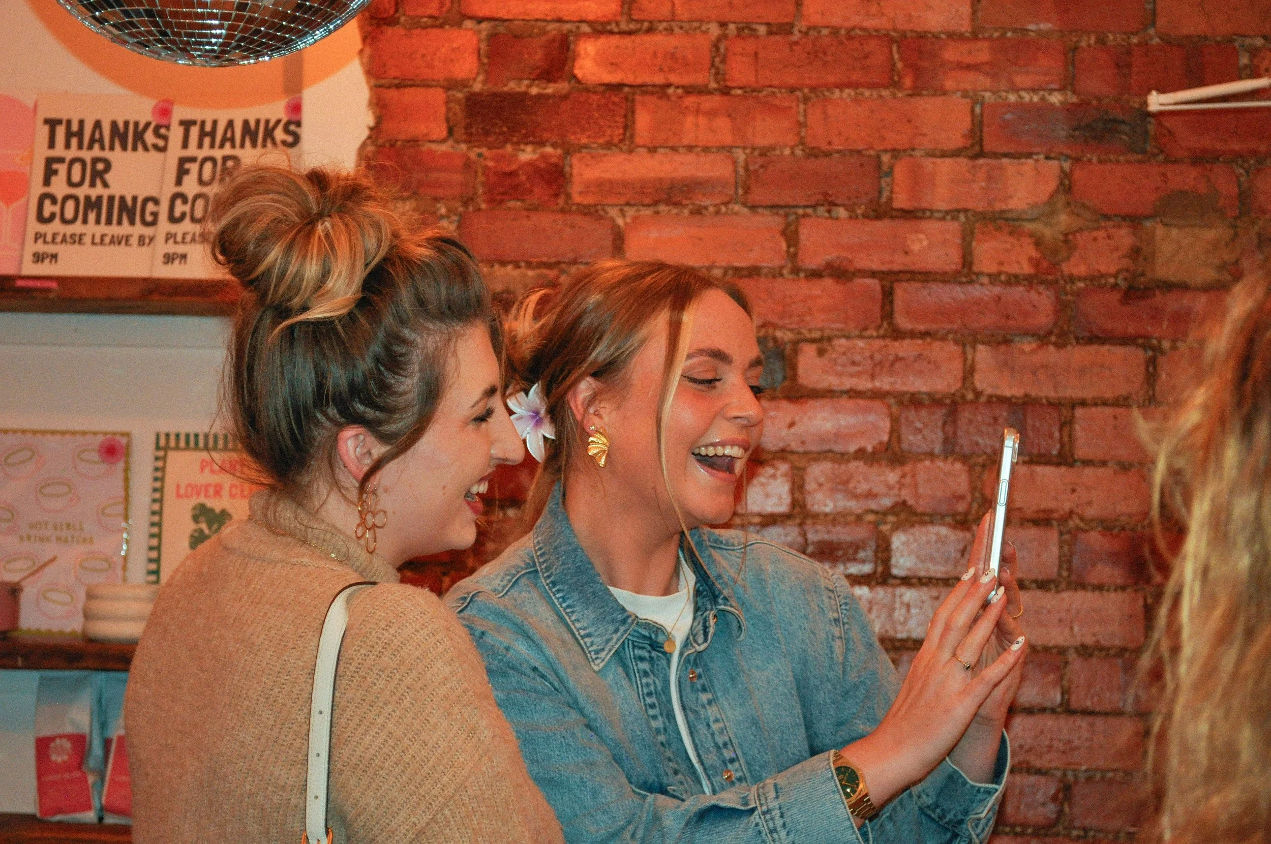 A couple of Creative Babes, laughing anf smiling warmly, whilst taking a mirror selfie together at a Creative Babes Club Studios Community Event.