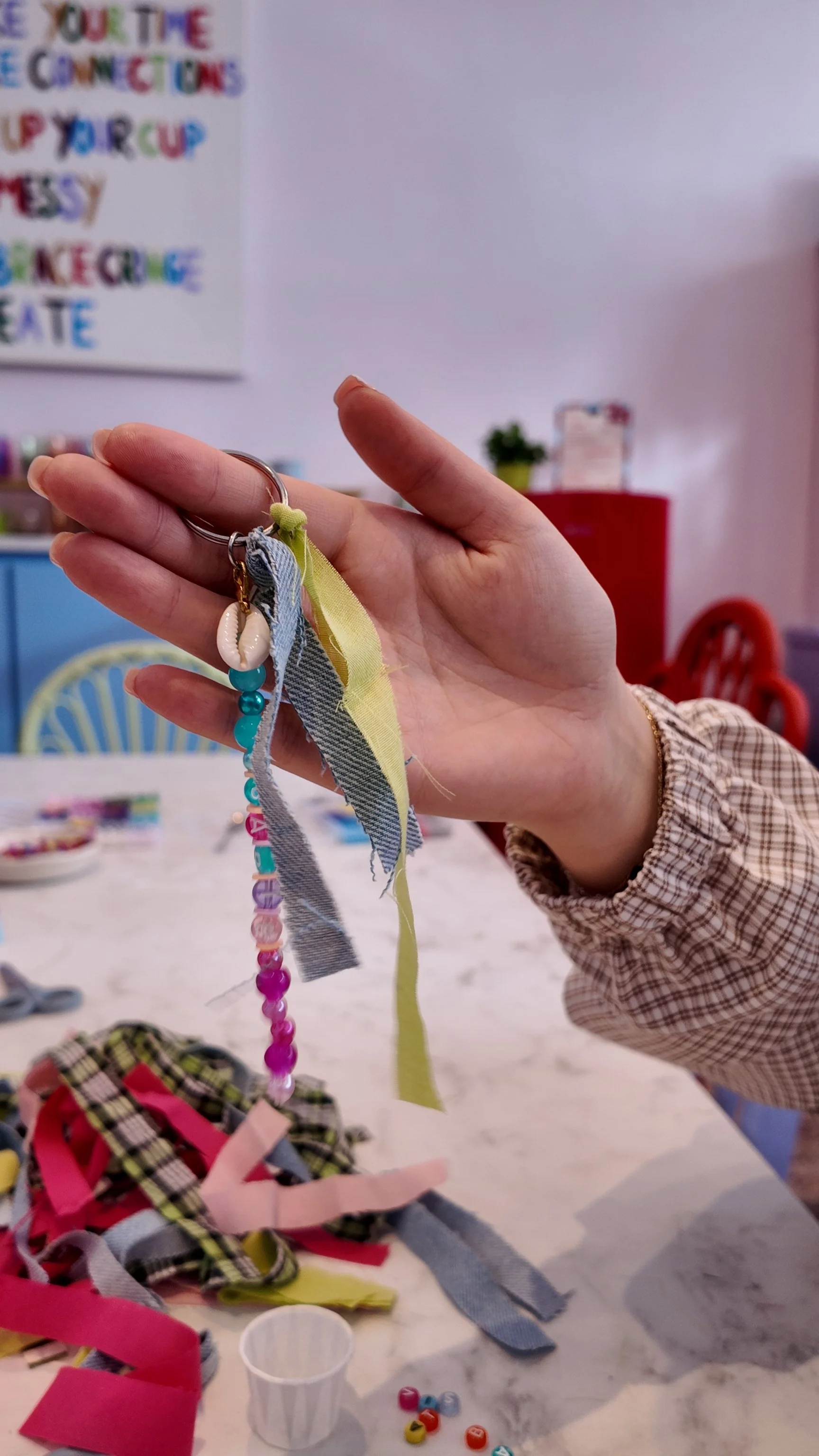 In the Studio, a Creative Babe holds up close a hand beaded Scrap Keyring that they made in our Workshop Atelier.