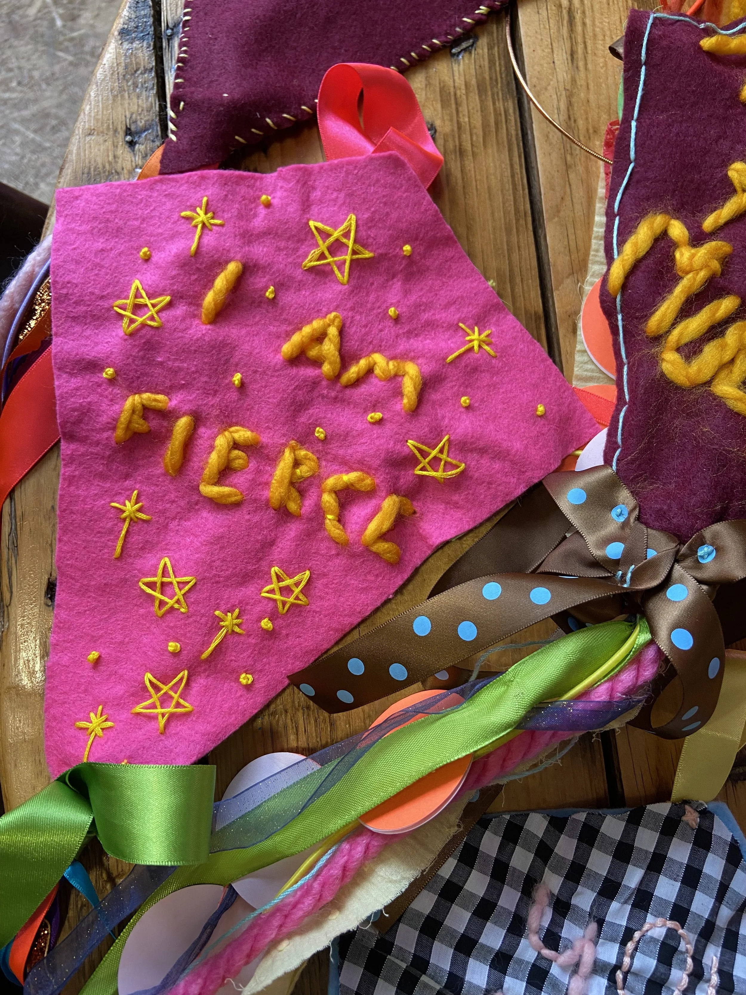 A Pile of Textiles, Felt Affirmation Kites made by Creative Babes for Redcar Kite Festival. The top Kite has a starry, hand stitched "I am Fierce" design in Hot Pink and Sunshine yellow.