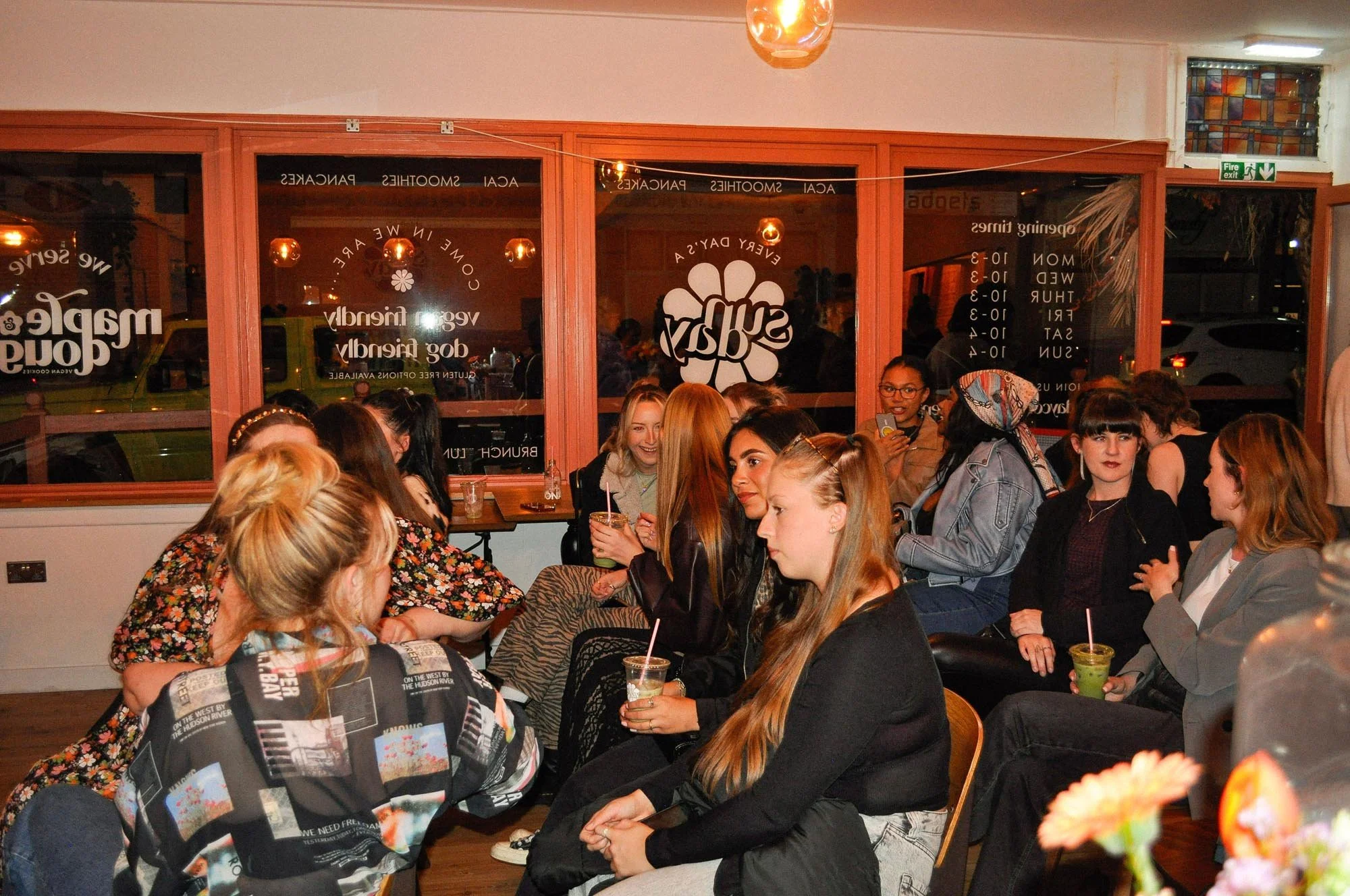 A group of women seated and chatting inside a cozy cafe or bar, with some holding drinks and others engaging in conversation.