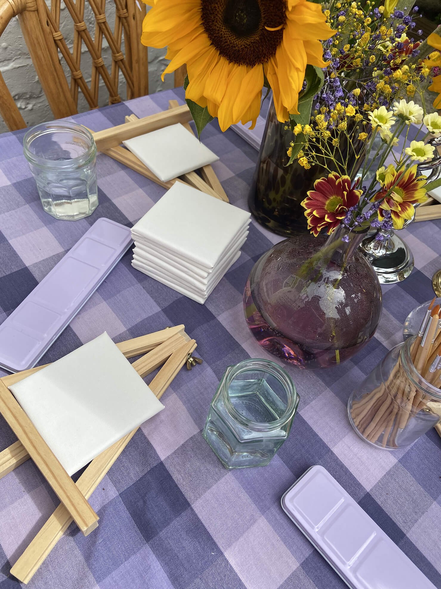 Table setting with flowers, napkins, and water glasses on a purple checkered tablecloth.