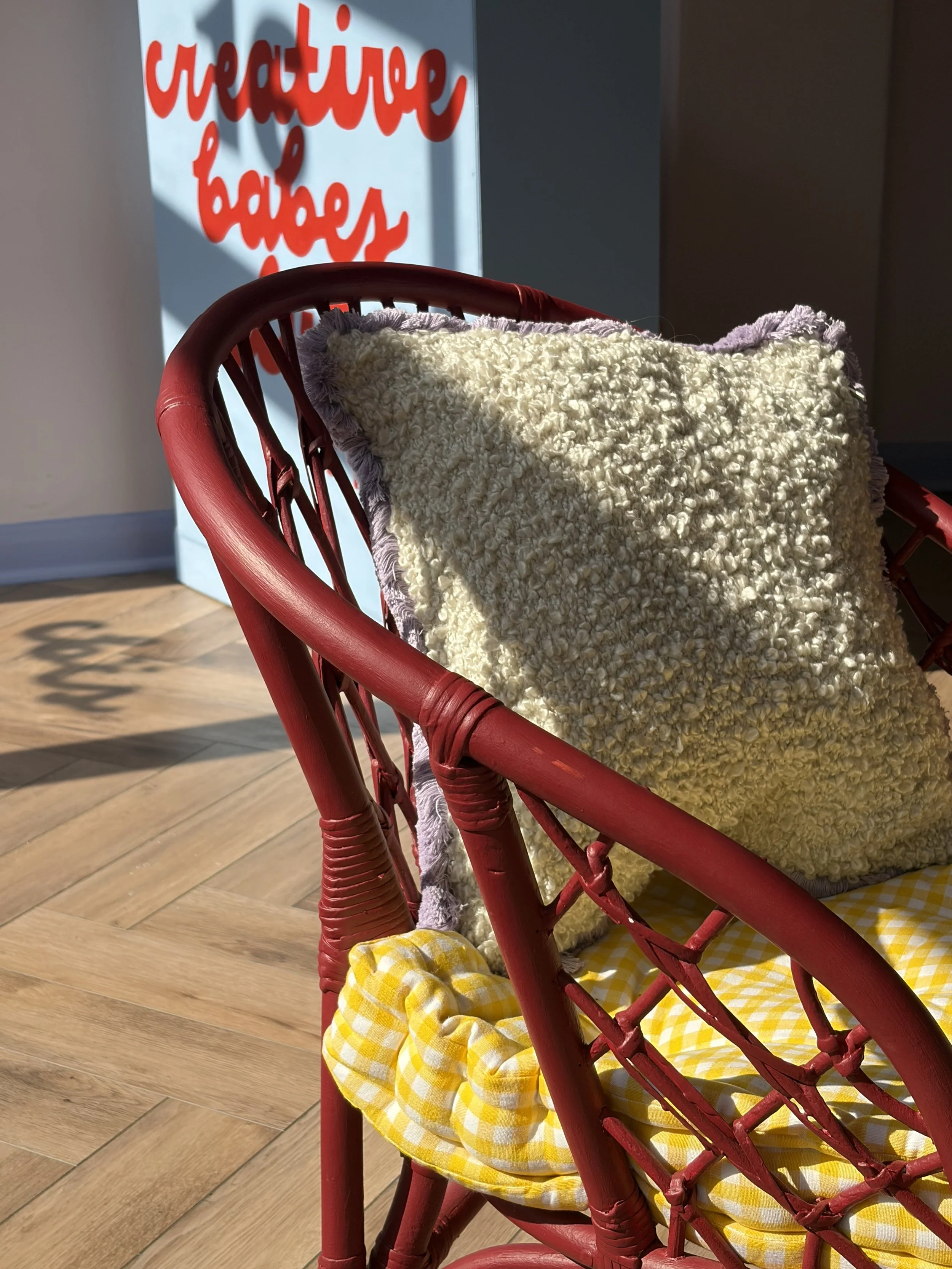 A close up of a comfy, gingham cushioned Burgundy Chair sits in the entranceway of our Studio.