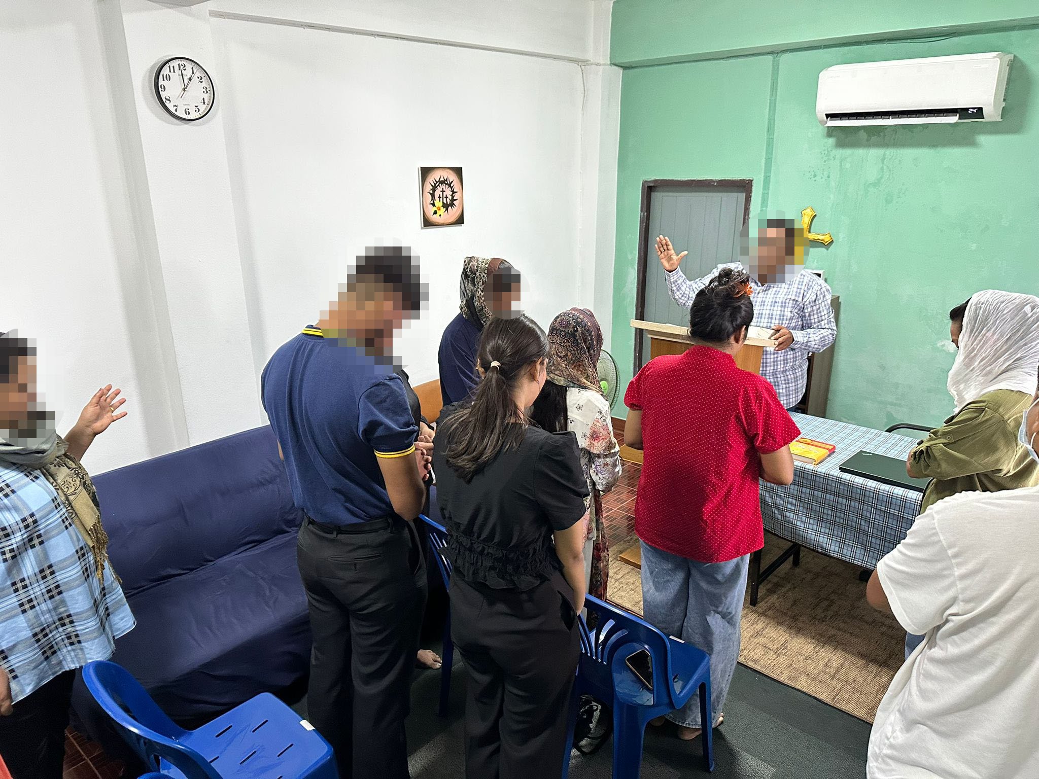 Mensen bidden en luisteren naar een spreker tijdens een religieuze bijeenkomst in een kleine kamer.