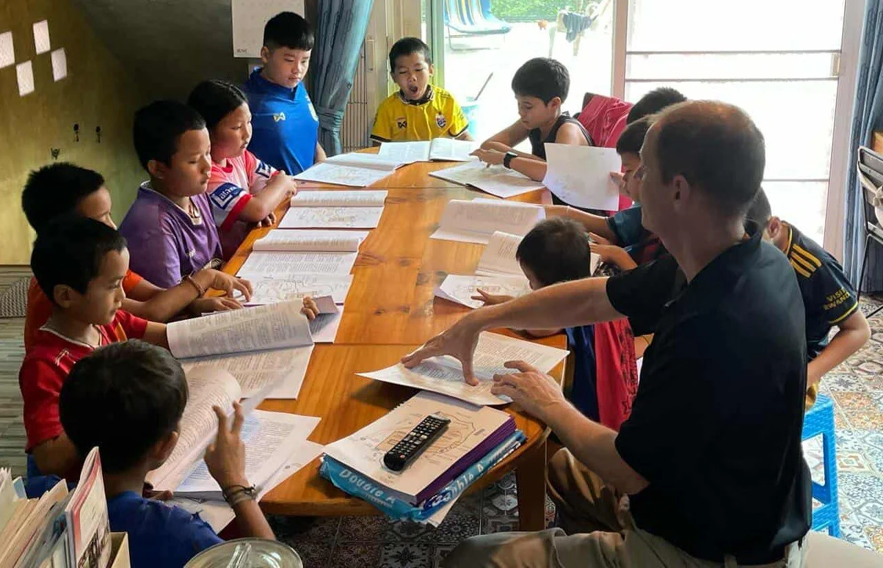 Leerkrachten en leerlingen zitten rond een tafel tijdens een leesactiviteit in een klaslokaal.