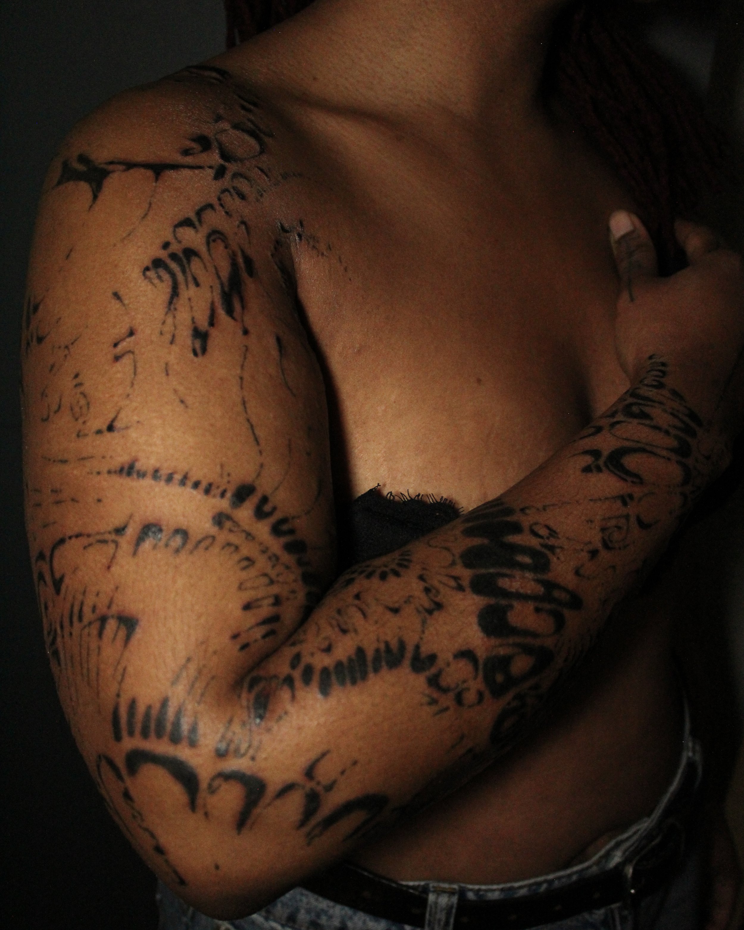 A person with tattoos on their arm and chest, shirtless, with a hand on their chest.