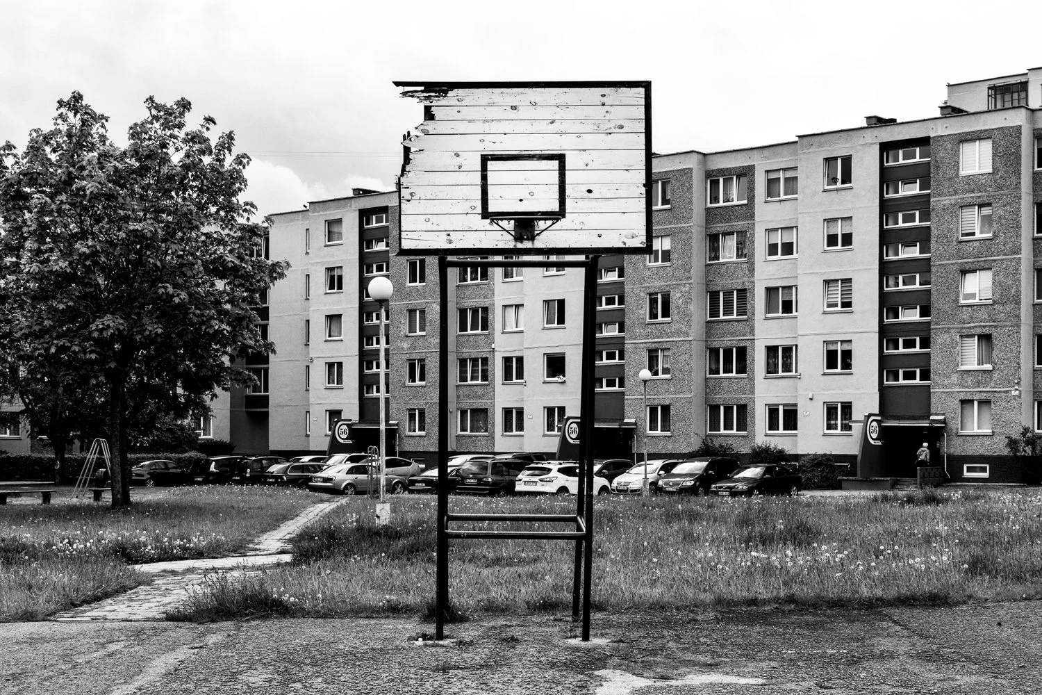 An empty outdoor basketball hoop with a worn backboard in front of a residential apartment building.