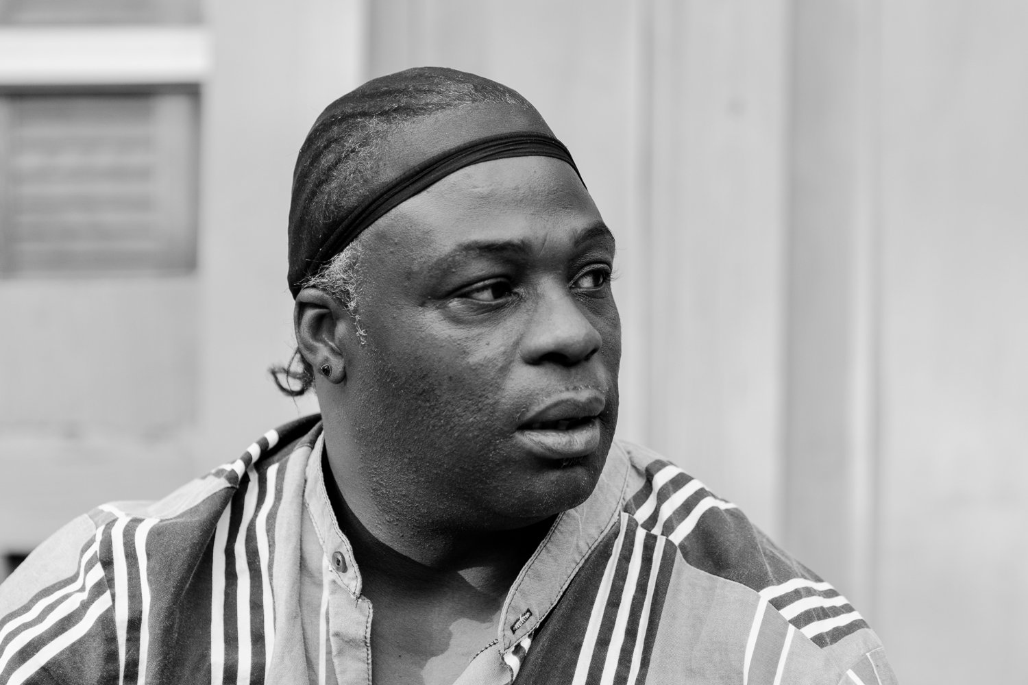 Black and white photo of a person with a head scarf and earrings, looking to the side, indoors.