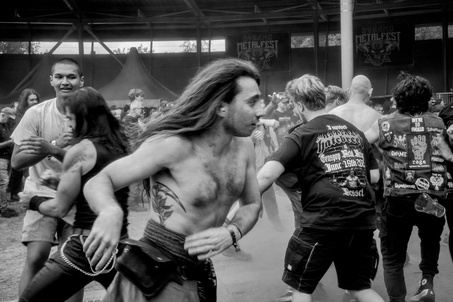 People dancing and having fun at a concert or festival, with a stage and banners reading 'Dynamo Metalfest' in the background, in a lively, energetic atmosphere.