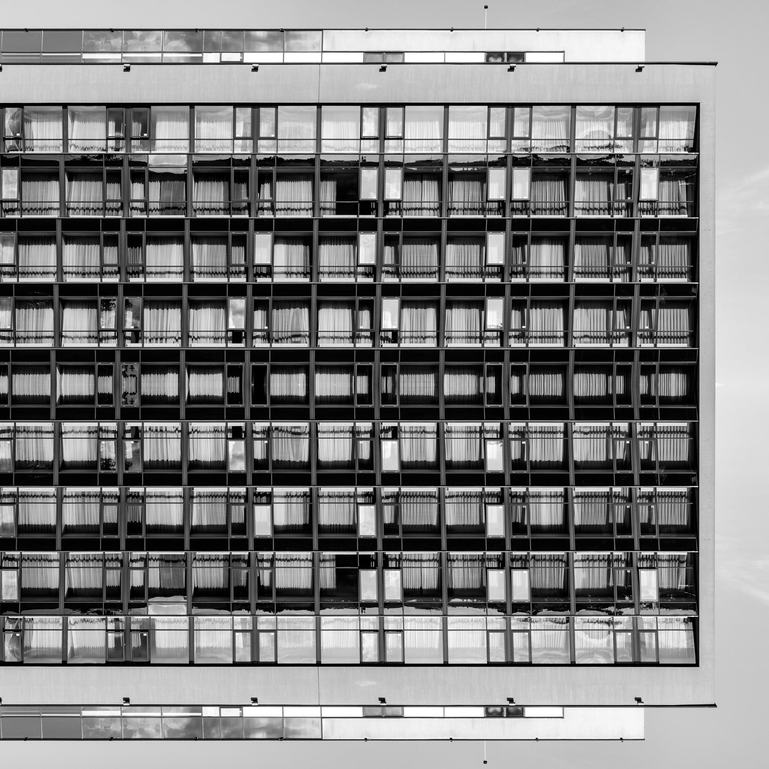 Black and white image of a modern multi-story office building with a grid of glass windows, some with curtains inside.