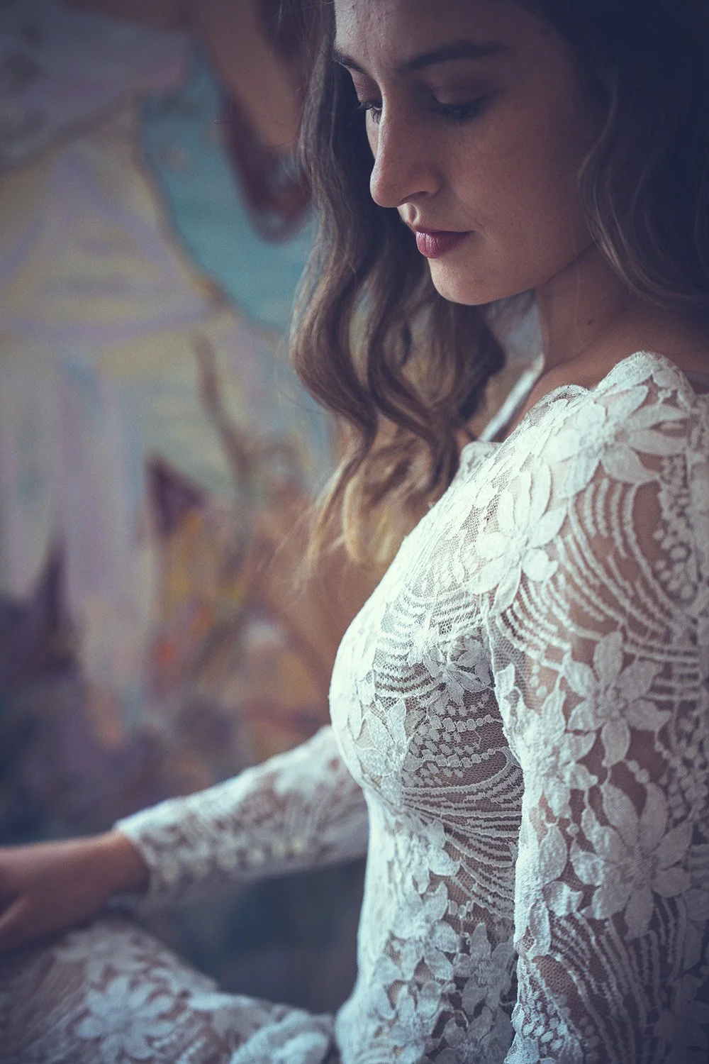 A bride in a white lace wedding dress with wavy hair sitting quietly, with her eyes closed and a serene expression.