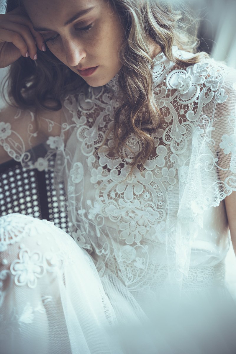 A bride with wavy brown hair wearing a white lace Tuesday's Bride wedding dress with floral embroidery.