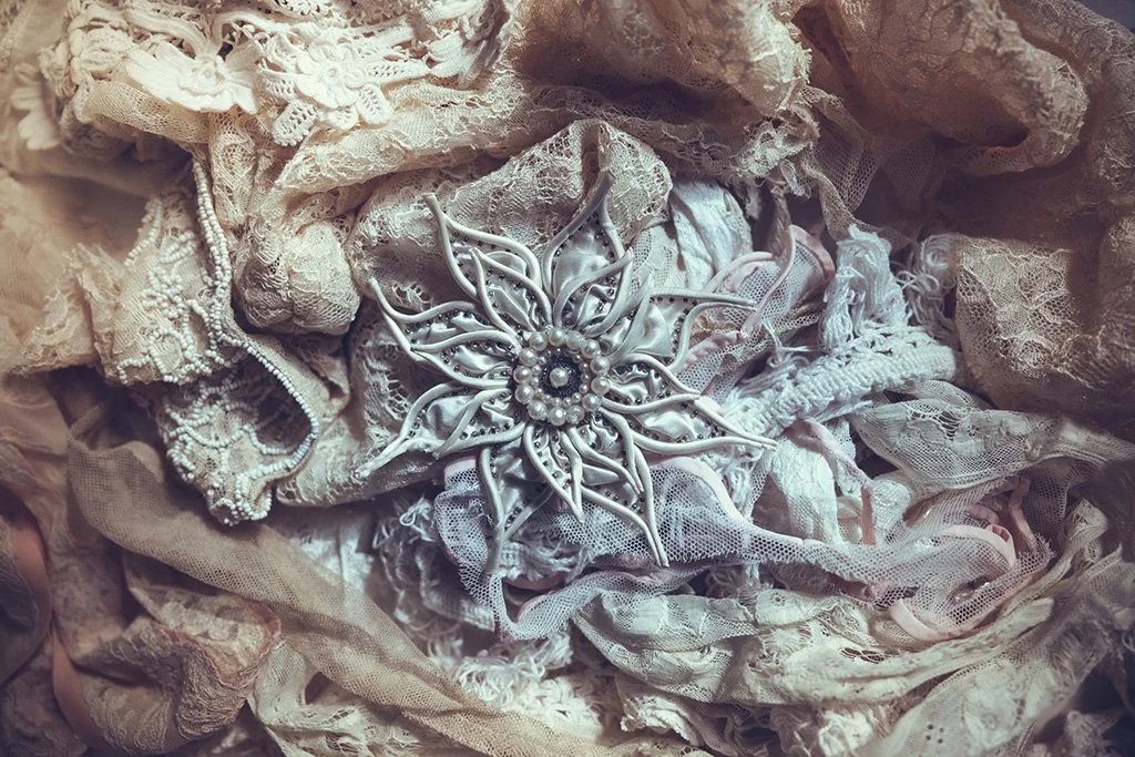 A decorative wedding brooch in the shape of a flower with pearl and rhinestone details, placed on a background of lace and fabric.