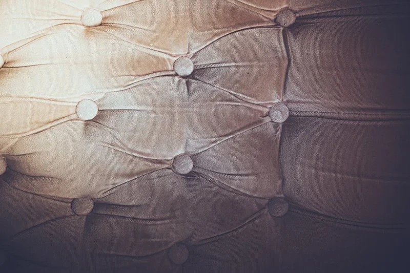 Close-up of a tufted upholstered fabric surface with buttons creating a diamond pattern.