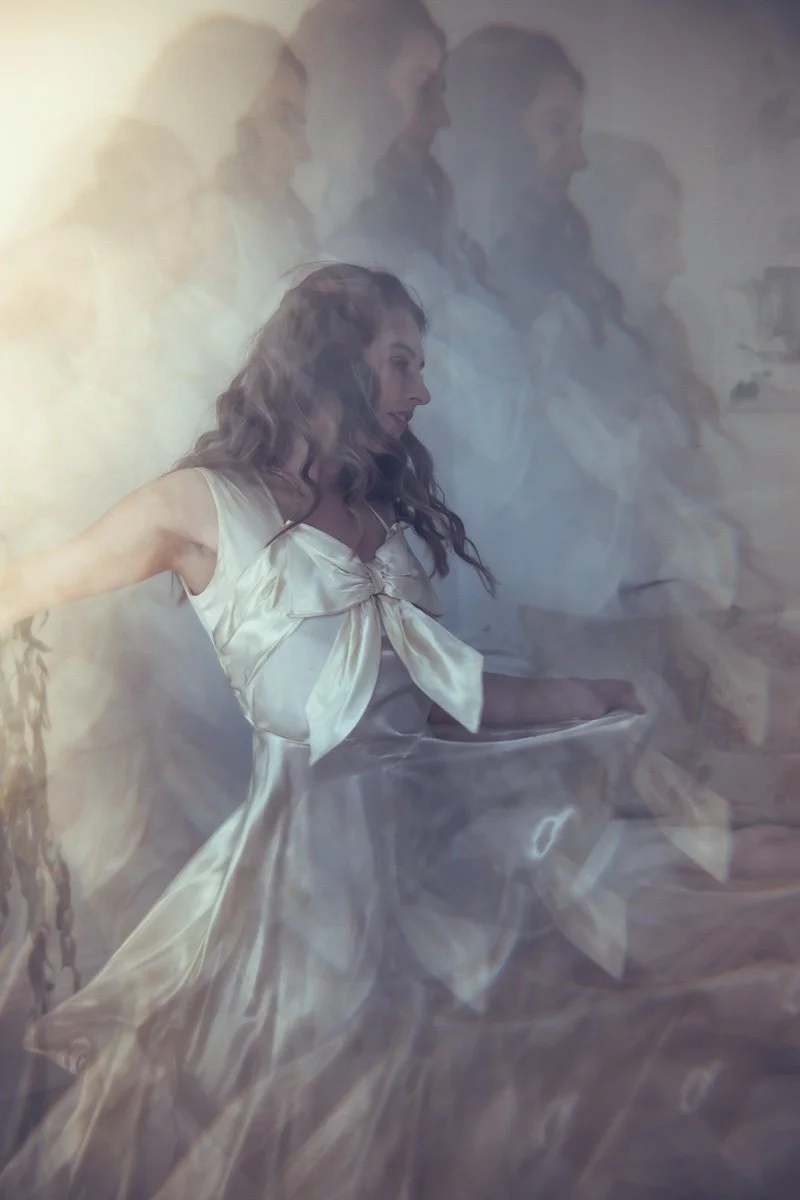 A woman in a flowing Tuesday's bride wedding dress with a large bow is spinning or dancing.