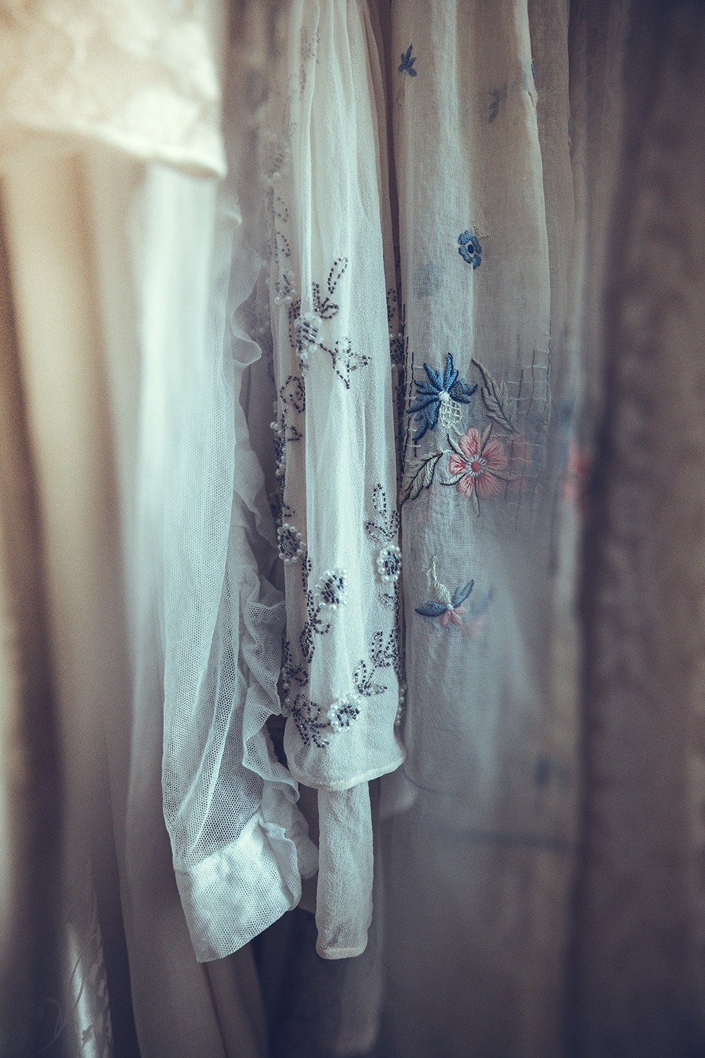 Close-up of embroidered and lace Tuesday's bride wedding dress with delicate floral and dragonfly design, hanging in a softly lit space.