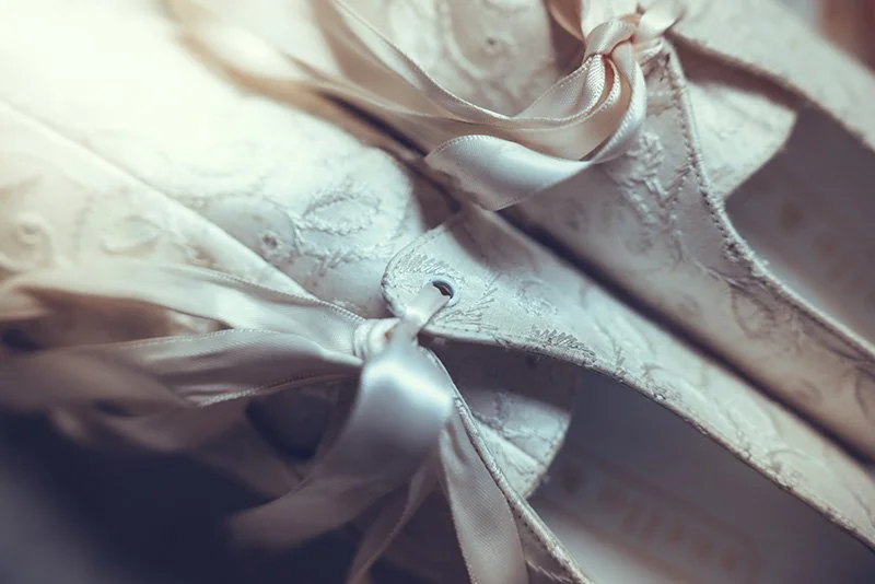 Close-up of a white wedding dress with intricate embroidery and satin ribbons.