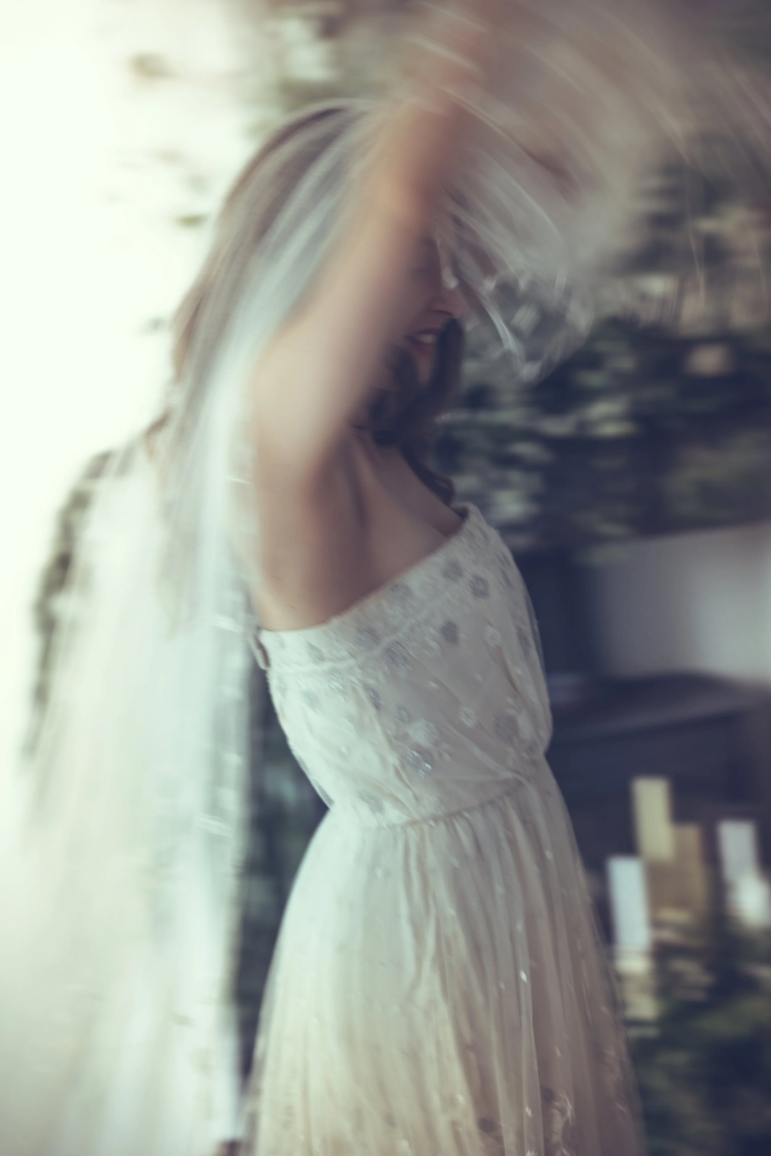 A woman in a white bridal gown standing indoors with a blurred background.
