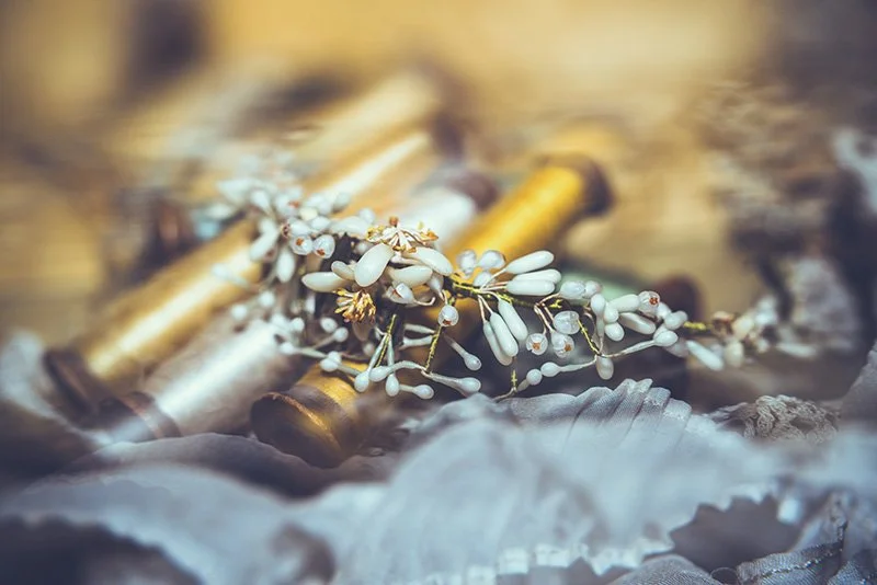 Close-up of a decorative branch with white beads and gold accents, placed on a fabric with a blurred background featuring gold-colored objects.