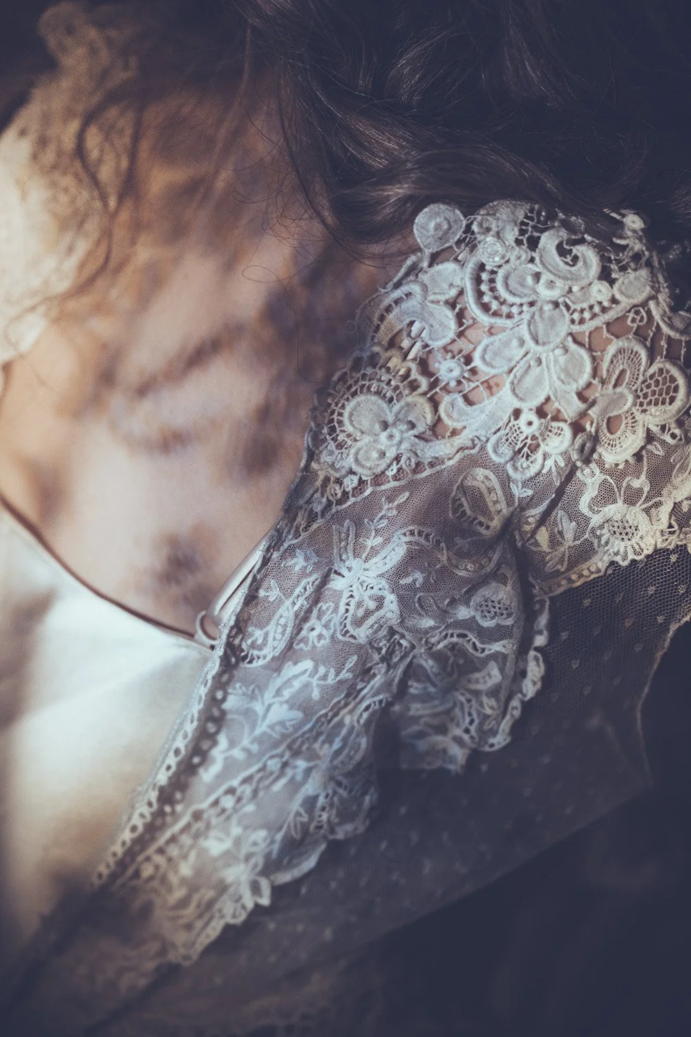 Close-up of a bride with closed eyes, wearing a wedding dress with intricate lace, floral embroidery.