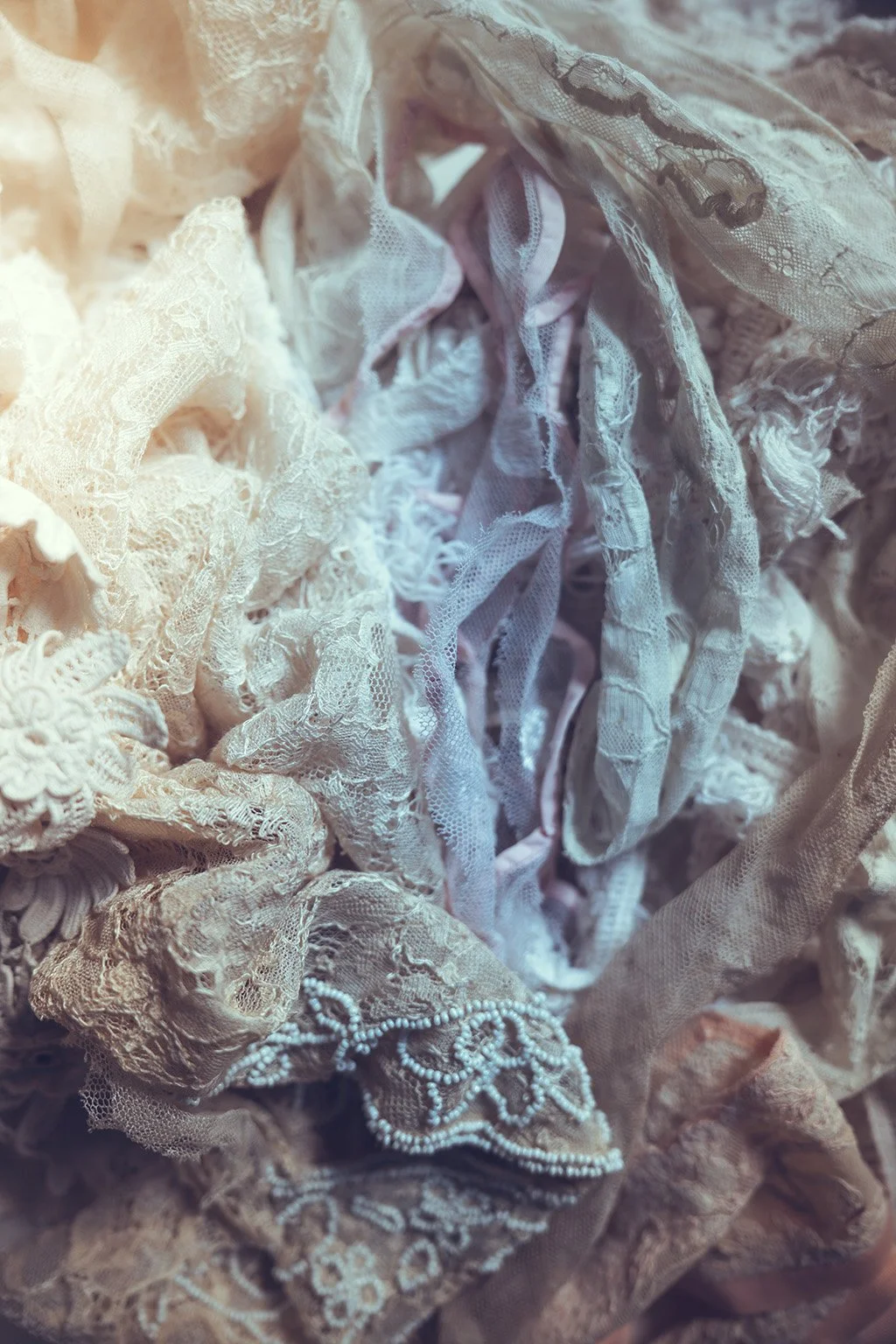 Close-up of tangled vintage lace and wedding fabric scraps in various light colours and intricate patterns.