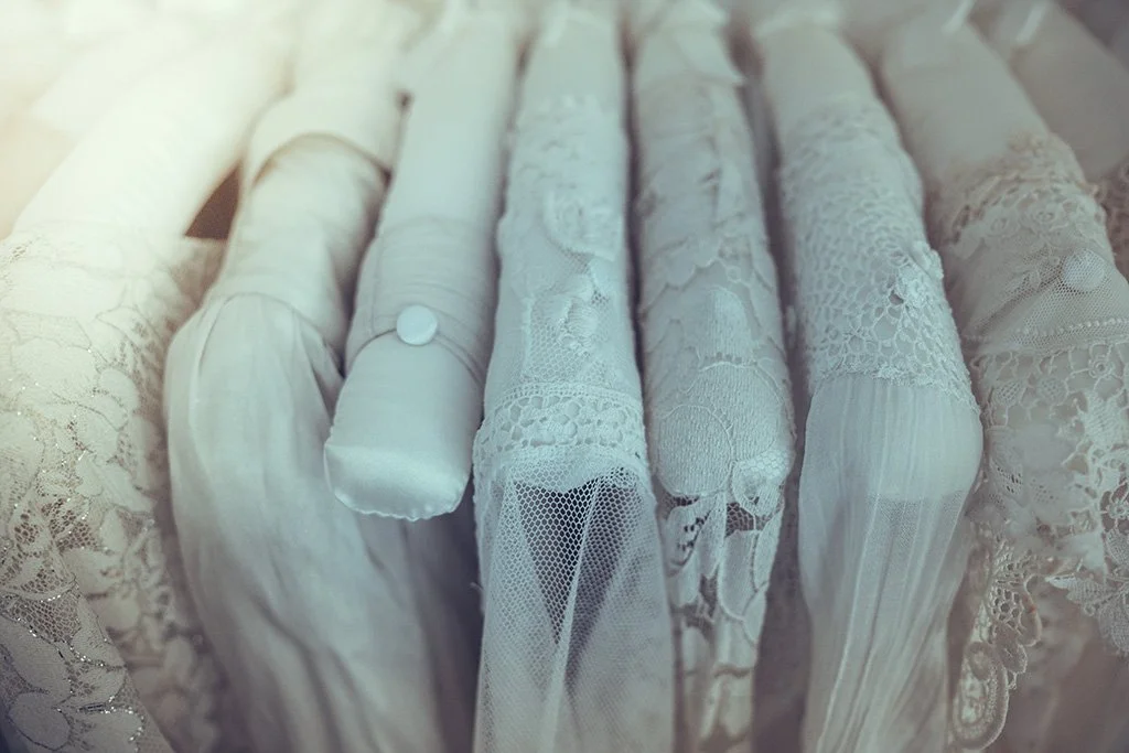 Close-up of a clothes rail with white lace and embroidered bridal gowns.