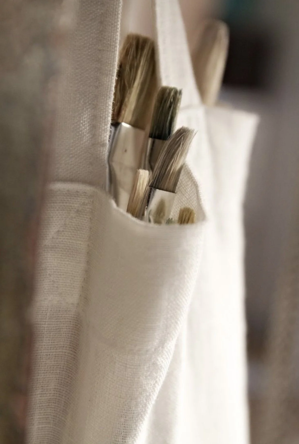 Close-up of paintbrushes with beige, gray, and brown bristles in a fabric wall organizer pocket.