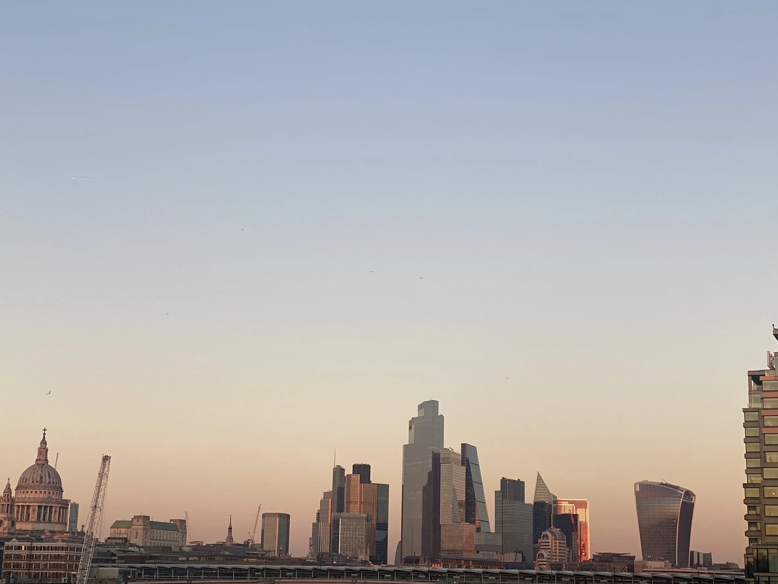 A city skyline at sunset featuring various modern skyscrapers and historic buildings, with a clear sky above in London.