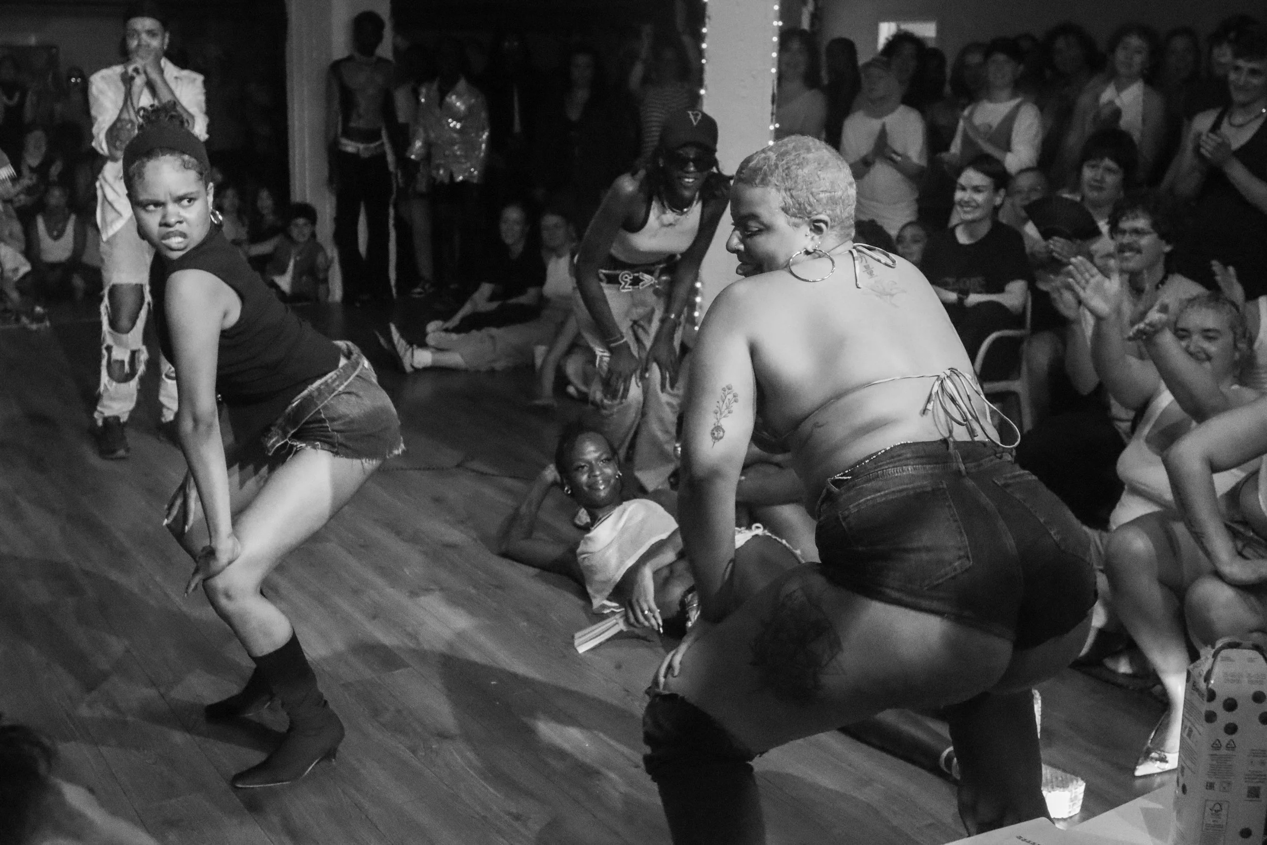 Two women dancing in front of an audience, with smiling spectators clapping and watching during a lively event.
