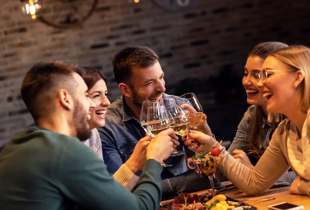 Eine Gruppe junger Menschen sitzt an einem Tisch im Kolmenhof, hält Weingläser und lacht miteinander bei einem gemütlichen Zusammensein.