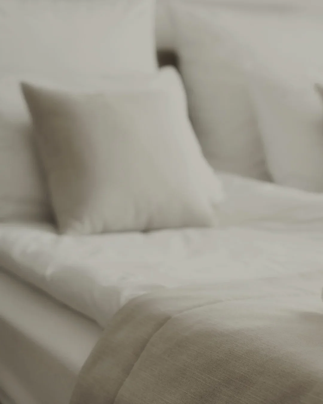 Weißes Bett mit mehreren weißen Kissen und einer weißen Bettdecke, schlicht und minimalistisch eingerichtet.