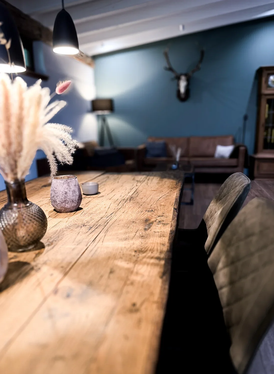 Innenaufnahme der Kolmenhof Business Lounge für fokussiertes Arbeiten mit einem rustikalen Holztisch, Kerzen und Dekorationen, im Hintergrund Ledersofas, ein Wanddeko-Hirschgeweih und eine Stehlampe.