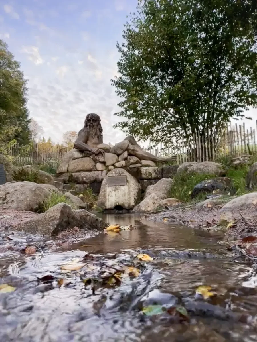 Ursprung der Donauquelle vor einer Statur, umgeben von Bäumen und Felsen nur wenige Schritte vom Kolmenhof entfernt.