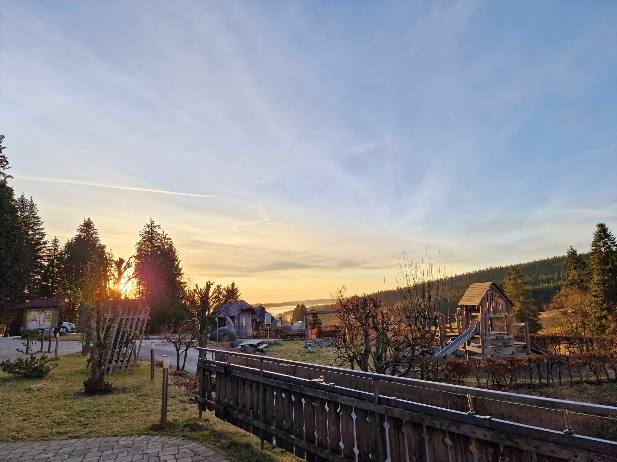 Blick auf einen Sonnenuntergang vom Kolmenhof aus, am frühen Abend, mit Bäumen und dem Kolmenhof Spielplatz in einer typischen Schwarzwald Umgebung, umgeben von Hügeln und Wäldern.