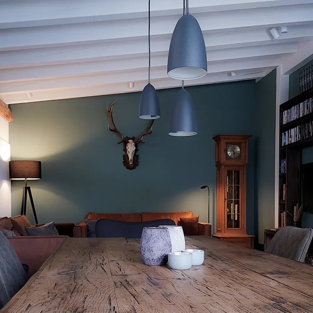 Die Kolmenhof Lounge für Rückzug und Verbindung mit natürlichen Materialien wie einem großen Holztisch, Wand dekoriert mit einem Geweih und einem Tierkopf, sowie einem Bücherregal.