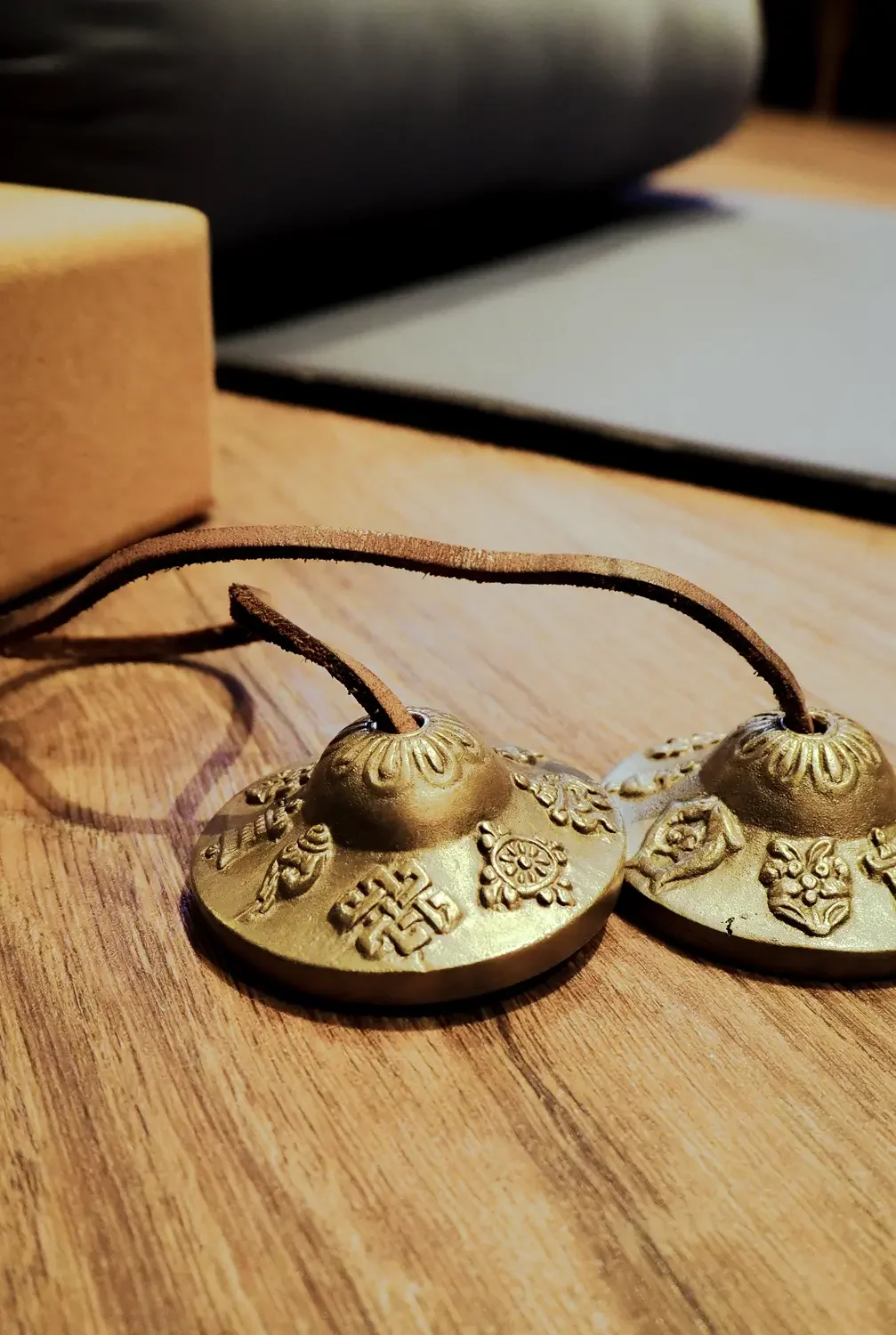 Ein Paar goldene buddhistische Klangschalen mit Lederriemen auf einem Holzboden im Yogaraum des Kolmenhofs.