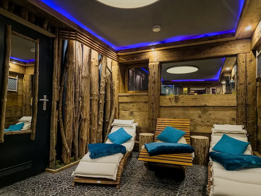 Die Kolmenhof Sauna mit Holzdekor, bequemen Liegen mit blauen Kissen und moderner Beleuchtung mit blauen LED-Lichtern.