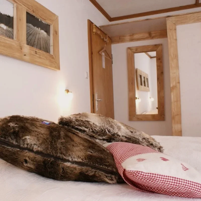Bett mit Fellkissen, Wandbilder, Spiegel und Holztüren in einem gemütlichen Kolmenhof Zimmer.