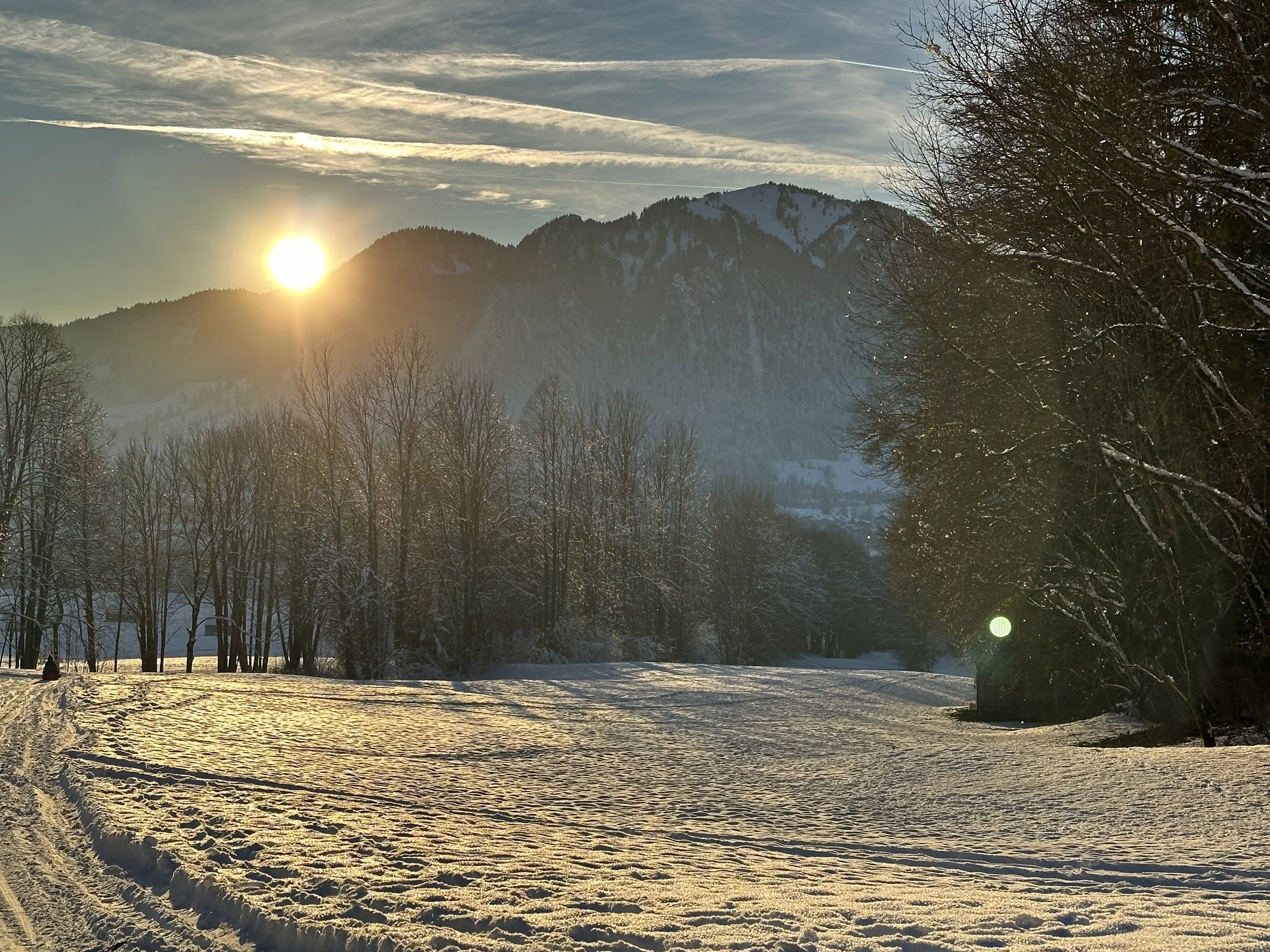 Sonnenuntergang über schneebedeutem Tal mit umliegenden Bergen und Bäumen.