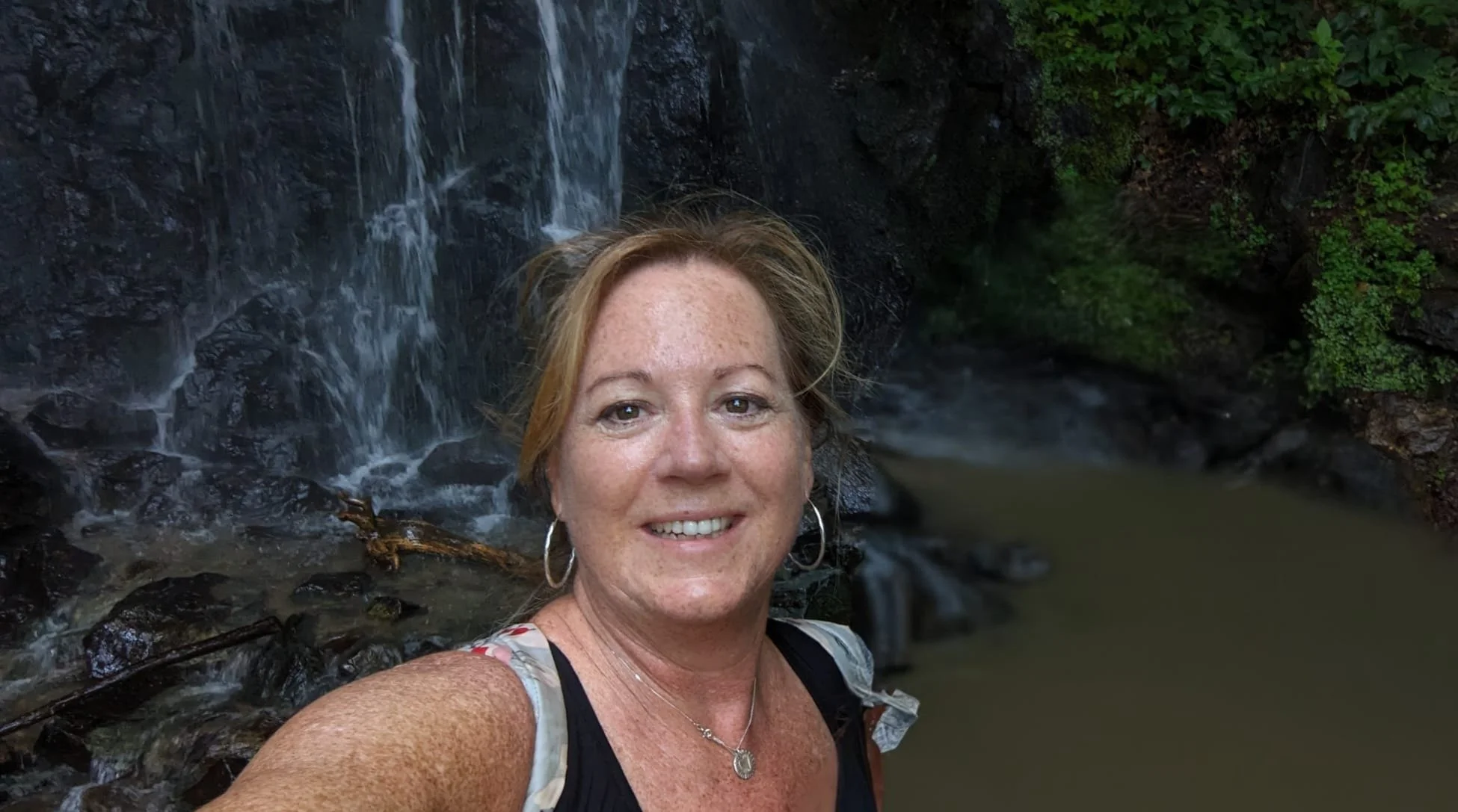 Flow Living embodiment coach smiling in front of a waterfall in nature