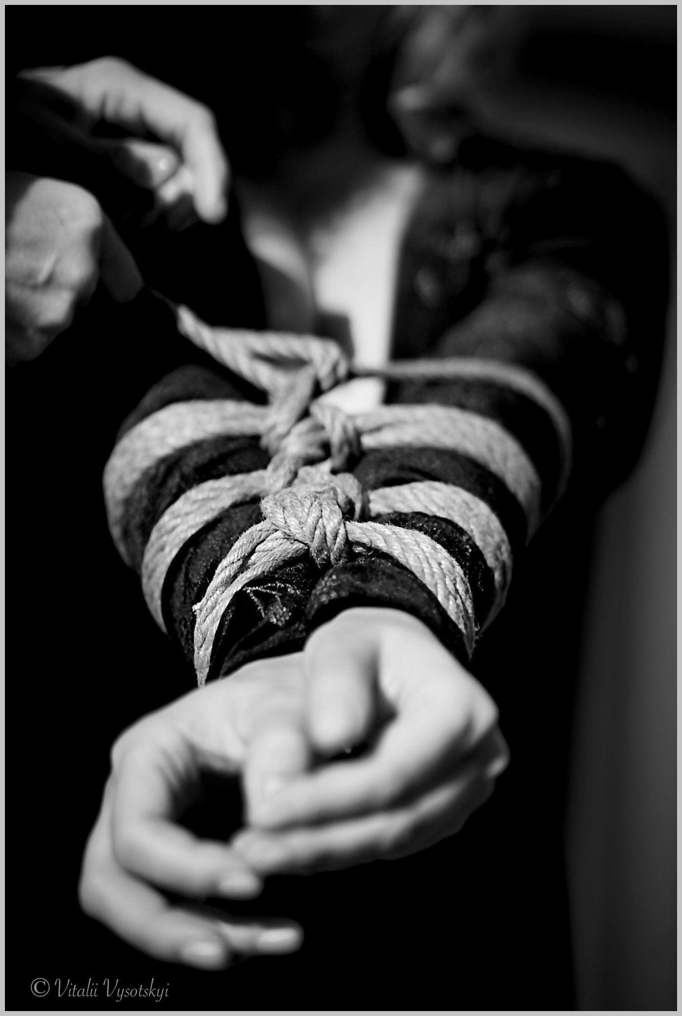 A person's arm is tied with multiple strips of cloth or fabric, and their hand is clenched into a fist.