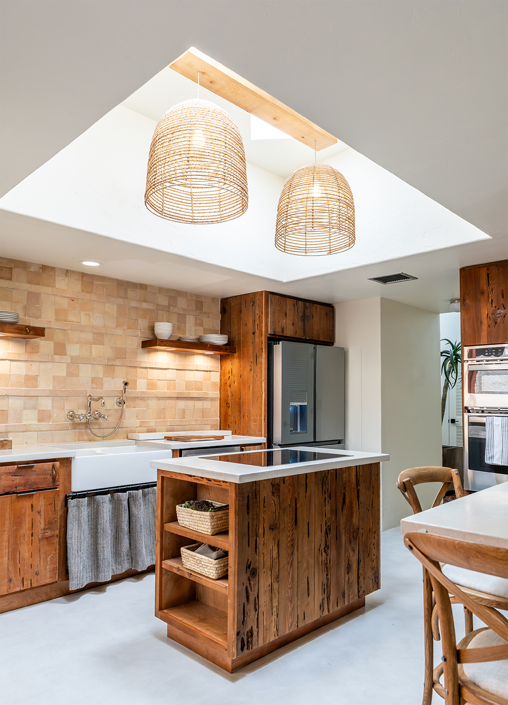 Kitchen with wooden cabinets, a kitchen island, beige tile backsplash, stainless steel appliances, and woven pendant lights hanging from a skylight.
