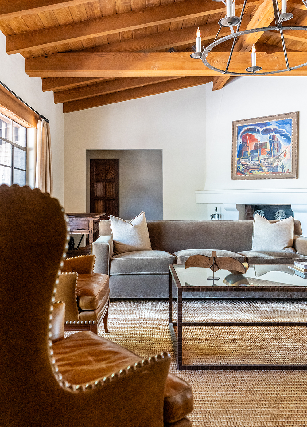 Living room with a wooden vaulted ceiling, a chandelier, a beige sofa with pillows, a glass coffee table, and art on the wall.