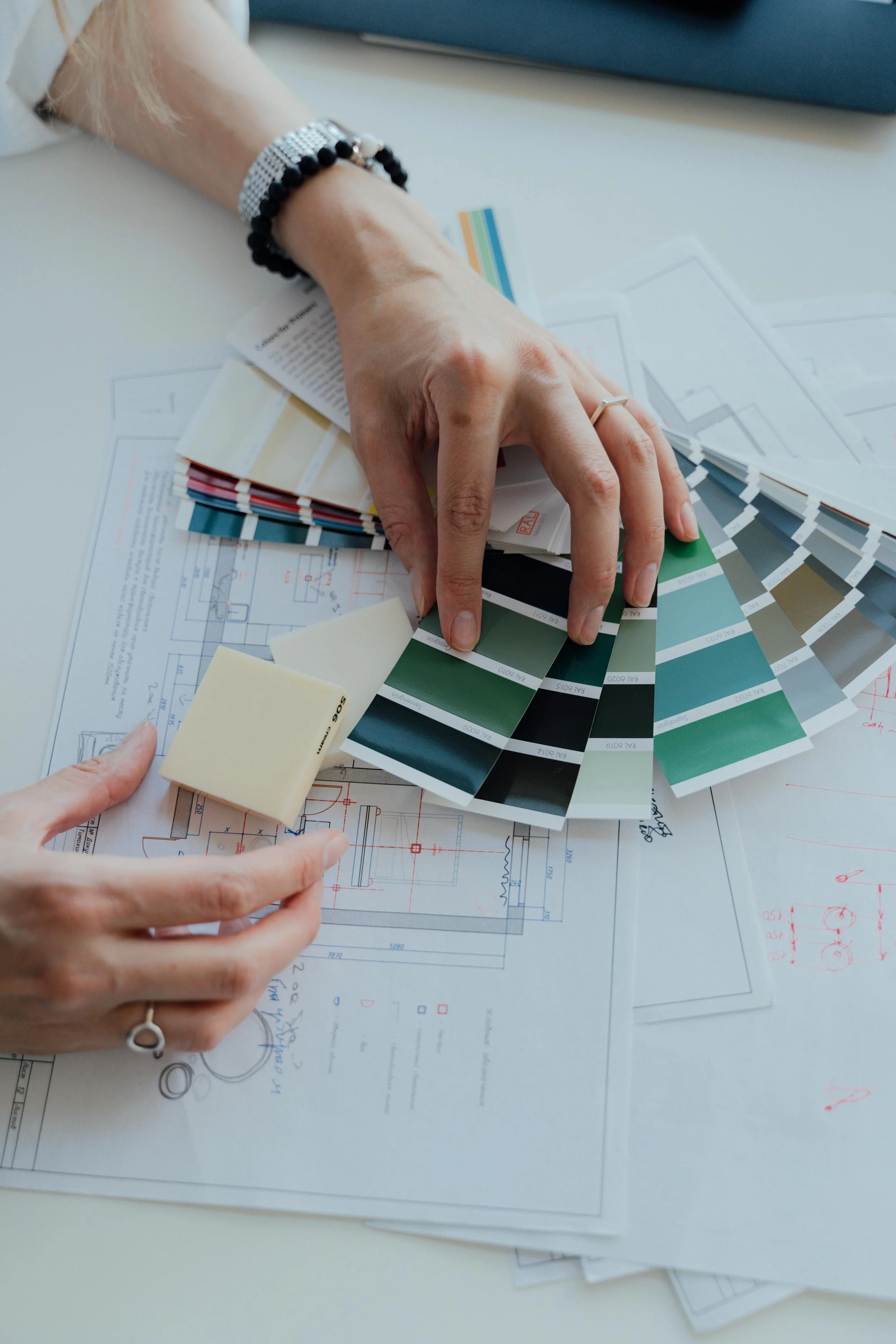 Person selecting paint color swatches over architectural blueprints on table.