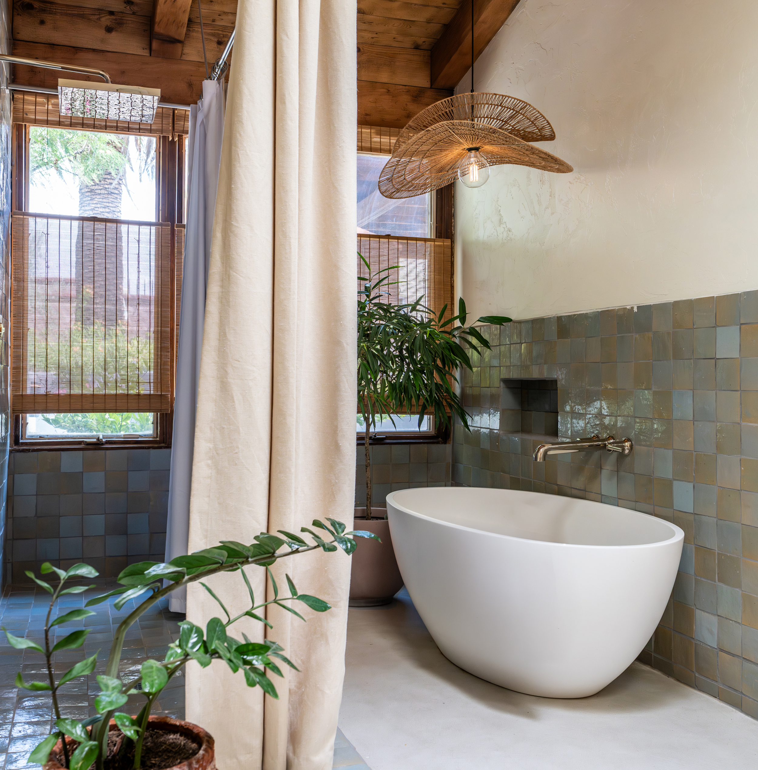 Modern bathroom with a freestanding bathtub, large windows with bamboo blinds, potted plants, and natural wooden accents.