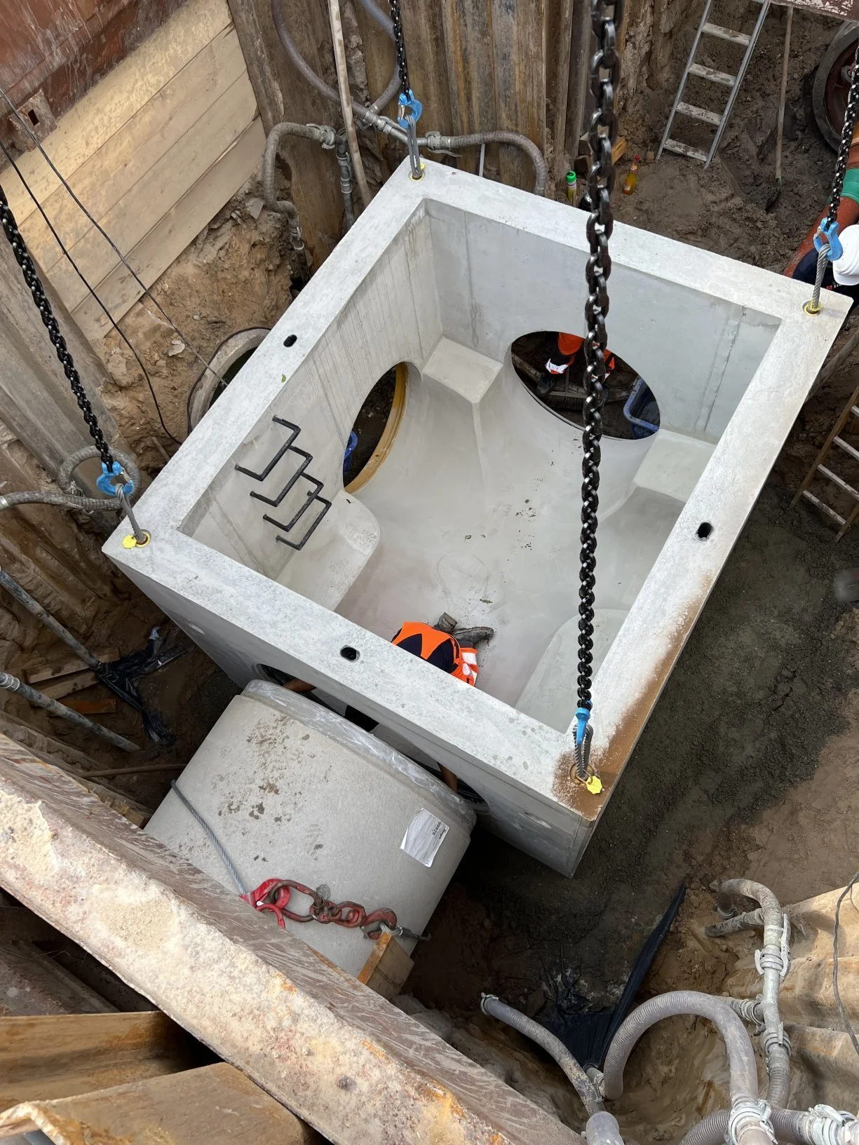 Bau einer Toilettenschüssel in einer Baugrube, mit Schläuchen, Seilen und Baummaterialien.