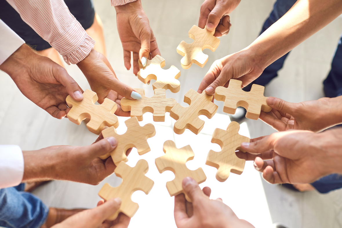 Multiple people assembling a puzzle with wooden puzzle pieces