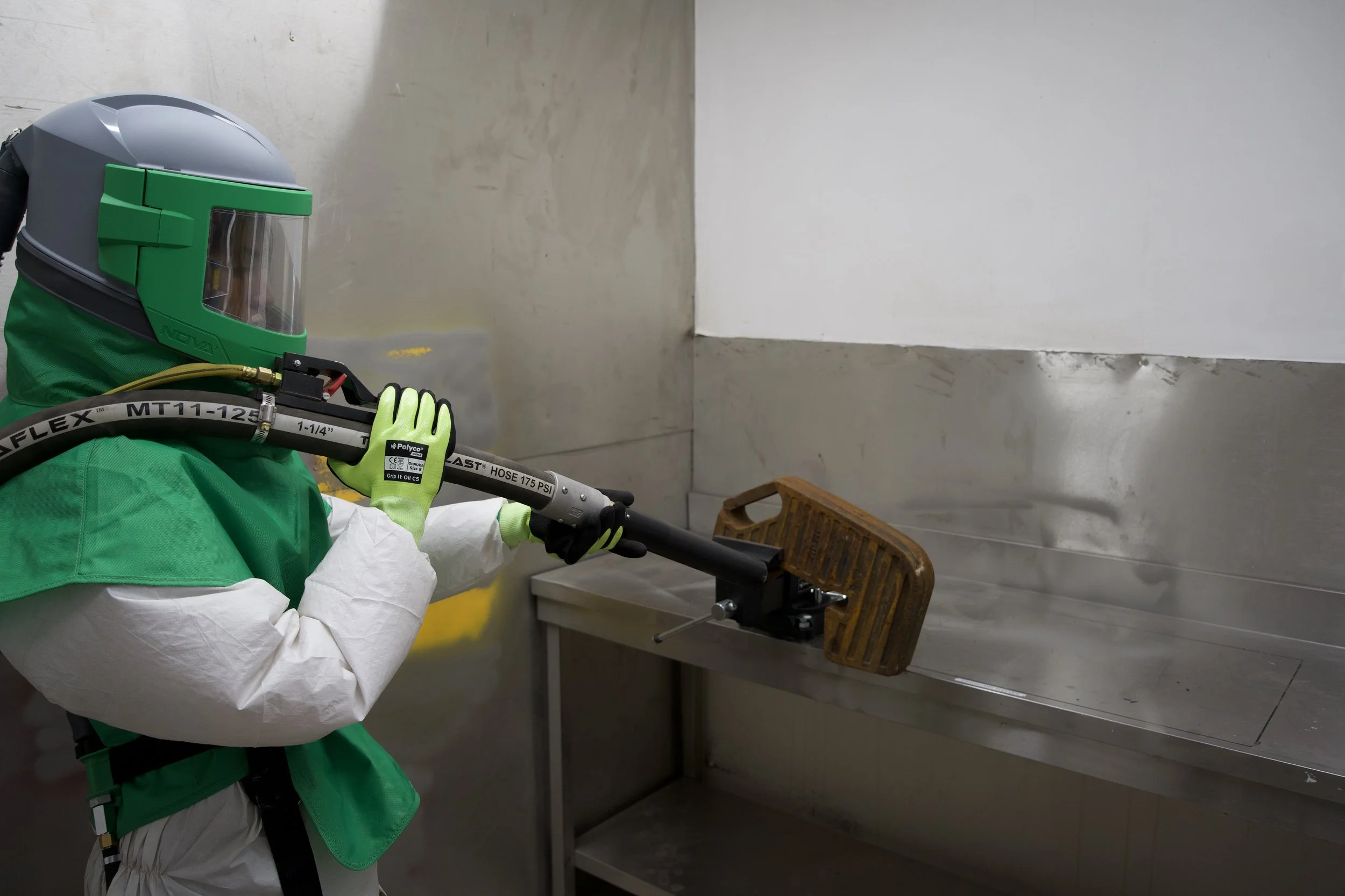 A worker in protective gear using a spray gun inside a metal room.